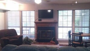 Una sala de estar con chimenea, un televisor montado en la pared y un ventilador de techo.