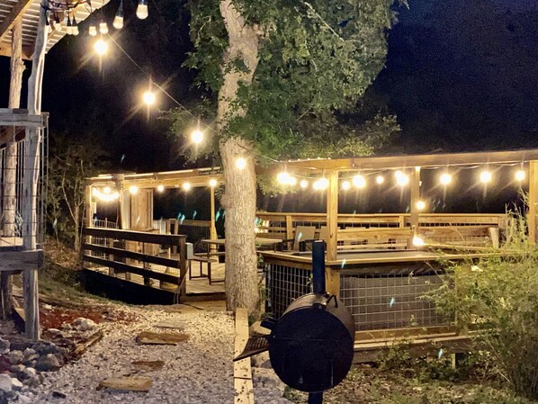 A wooden deck with string lights, outdoor seating, and a grill area.