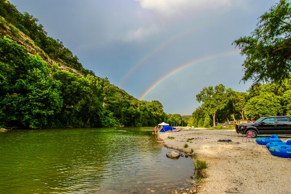 A riverbank with a tent, a car, and blue rafts. - 2 Cozy private cabins rent together - outdoor kitchens, hot tub, & RIVER ACCESS! (New Braunfels)