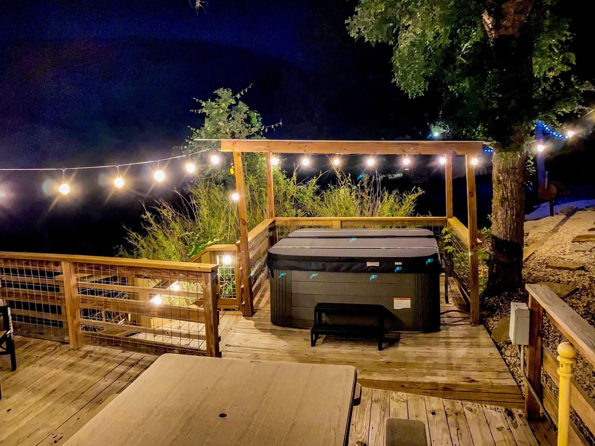 A wooden deck with a hot tub, string lights, and a wooden fence.