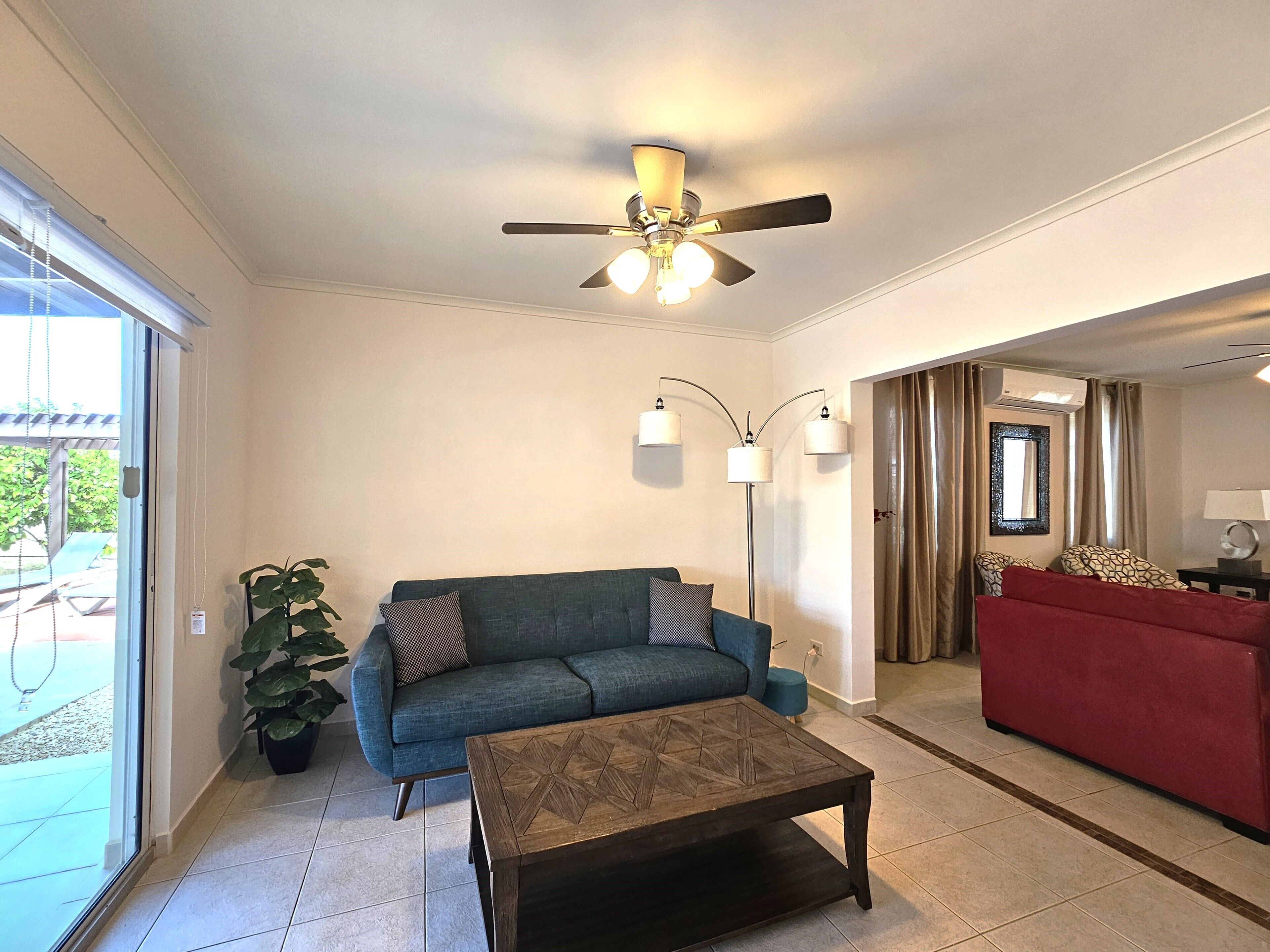 A living room with a blue sofa, a wooden coffee table, a ceiling fan, and a red sofa.