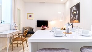 Ett modernt kök med en central köksö, en matplats med stolar, en kaffestation och en platt-TV på väggen.