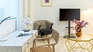 Ett rum med ett skrivbord, två stolar, en tv, en vas med blommor och ett geometriskt format soffbord.