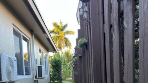 Ein schmaler Weg, der von einem Haus und einer Holzzahlung gesäumt wird, mit einem kleinen Garten und Außengeräten zur Klimatisierung.