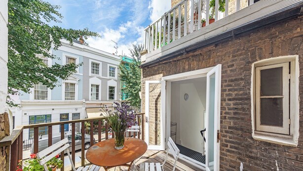 A wooden deck with a round table and white chairs, a potted plant, and a view of neighboring buildings. - Notting Hill Chic, by Veeve (London)