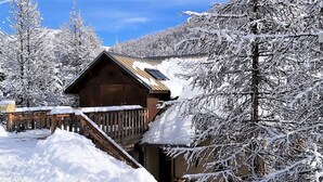A wooden cabin with a sloped roof, surrounded by snow-covered trees and a wooden fence.