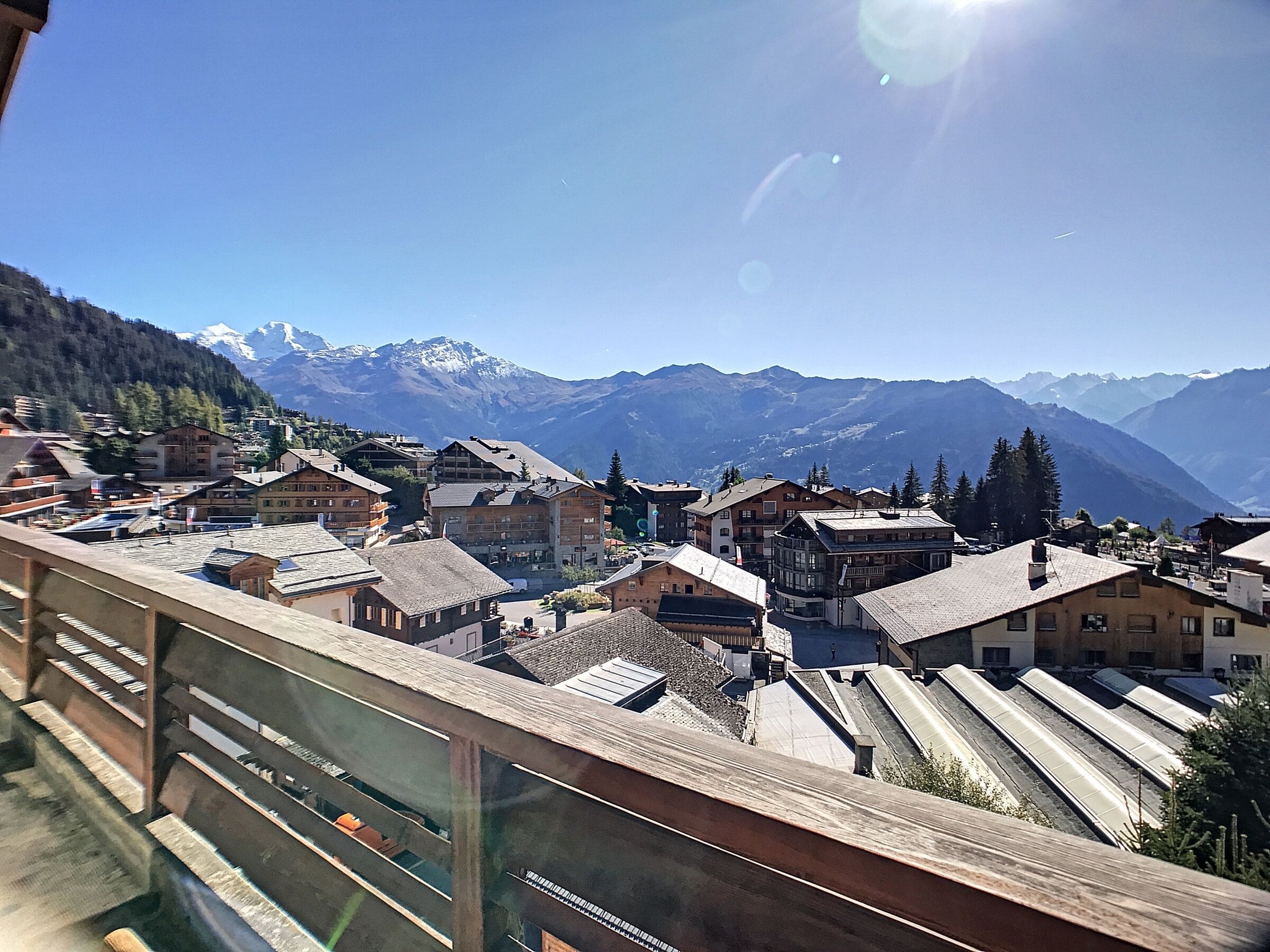 A mountain town with traditional wooden buildings, a clear sky, and snow-capped mountains in the background.