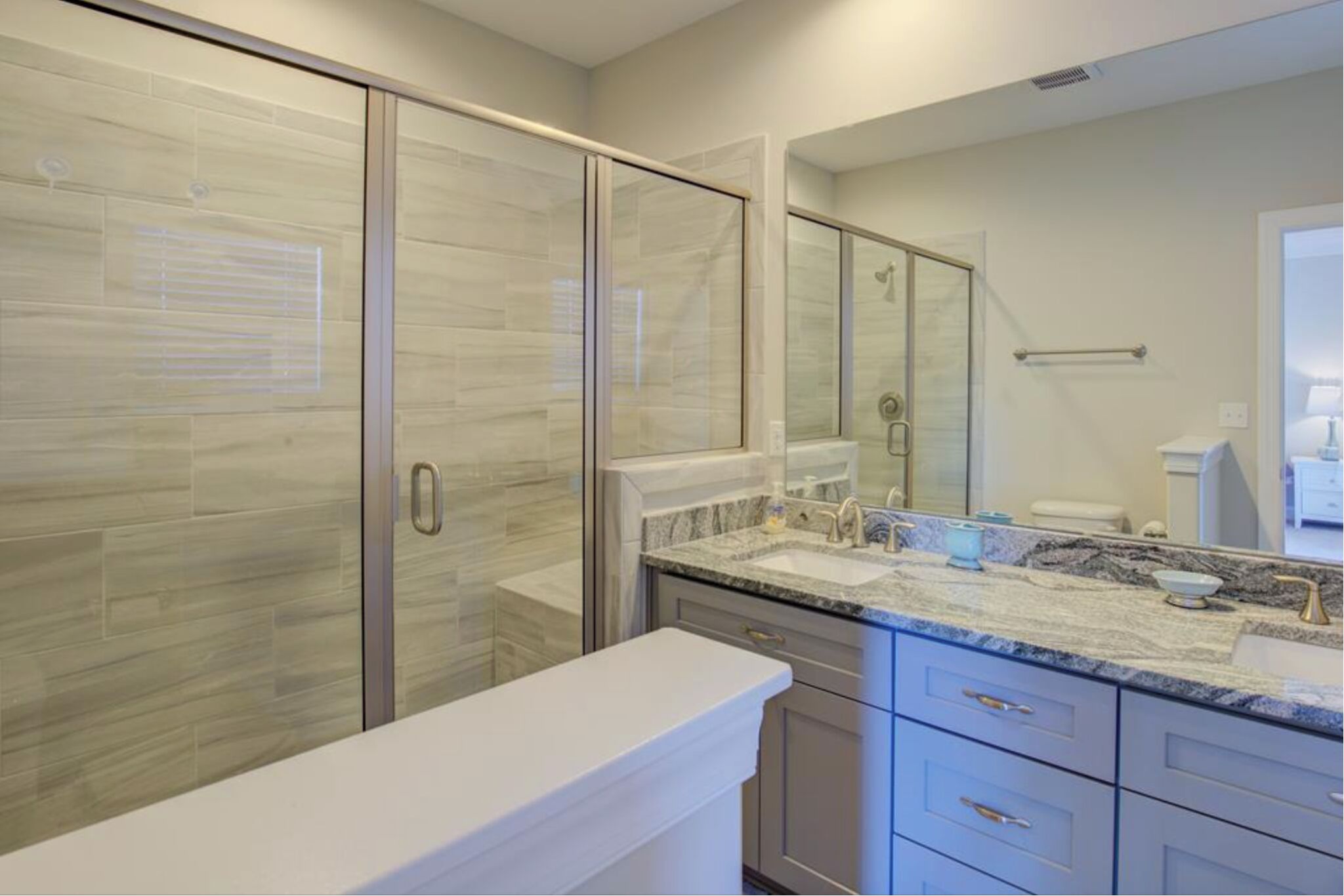 Une salle de bain moderne avec une douche à parois de verre, un lavabo surmonté d’un plan de travail en marbre et un grand miroir.
