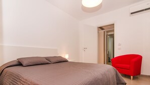 A bedroom with a large bed, a red chair, and a door leading to another room. - hilde's house 2 (Scicli)