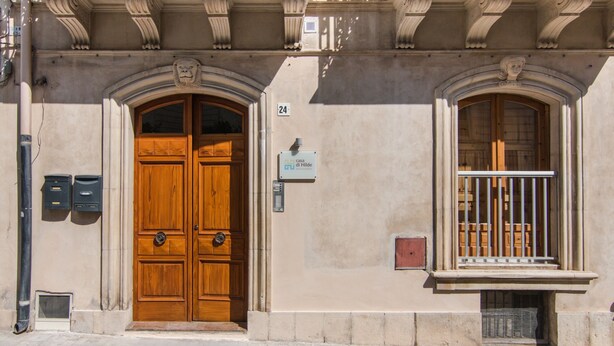A building with a large wooden double door, a small balcony with a metal railing, and a mailbox on the wall. - hilde's house 2 (Scicli)