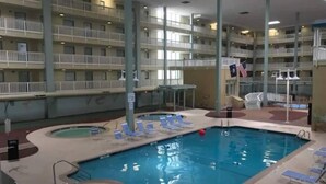 En indendørs swimmingpool med flere balkonniveauer, liggestole og et flag.