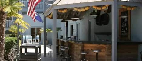 Un espace bar extérieur au design rustique, comprenant un comptoir en bois et des tabourets.