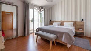 Ein Schlafzimmer mit einem großen Bett, einer Bank, einem Kleiderschrank und einer Glastür, die auf einen Balkon führt.