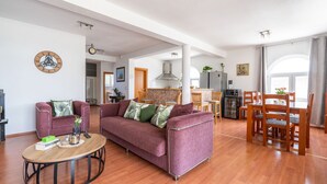 Ein großzügiger Wohnbereich mit einer Couch, einem Couchtisch und einem Esstisch. Im Hintergrund ist eine Küche zu sehen.