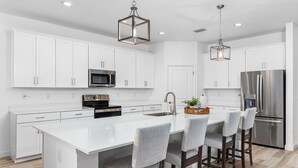 A modern kitchen with white cabinetry, stainless steel appliances, and a central island with bar stools. - Great Location! 2,444 sq ft canal front villa with heated pool/spa. (Cape Coral)