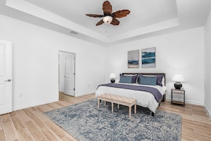 Quarto com cama, mesas de cabeceira, um banco, ventoinha no teto e obras de arte na parede.