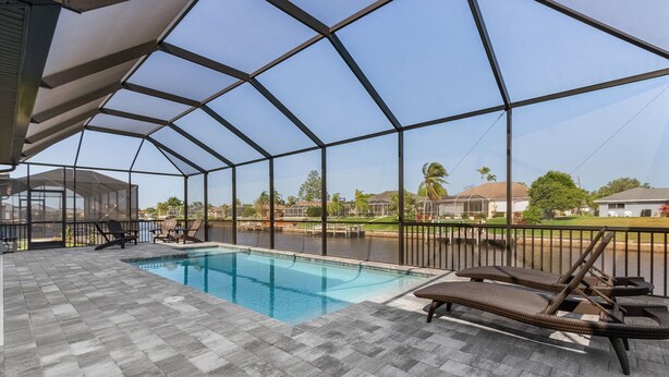 A covered outdoor swimming pool with lounge chairs, a patio area, and a view of a residential neighborhood. - Great Location! 2,444 sq ft canal front villa with heated pool/spa. (Cape Coral)