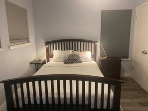 Une chambre à coucher comprenant un lit, des tables de chevet, une commode et un luminaire fixé au mur.