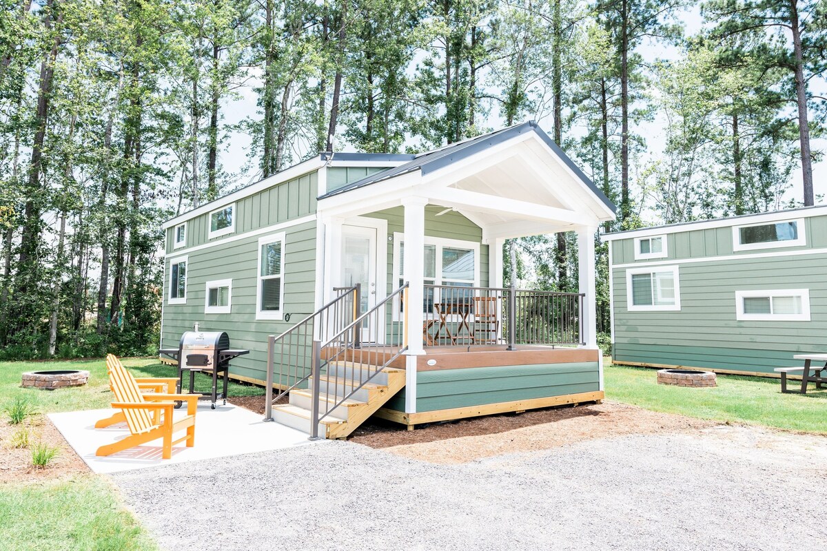 A two-story cabin with a covered porch, a grill, and a fire pit.