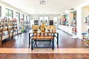 A spacious store with wooden flooring, shelves stocked with various products, and a central display table with packaged goods. - Carolina Pines (Conway)