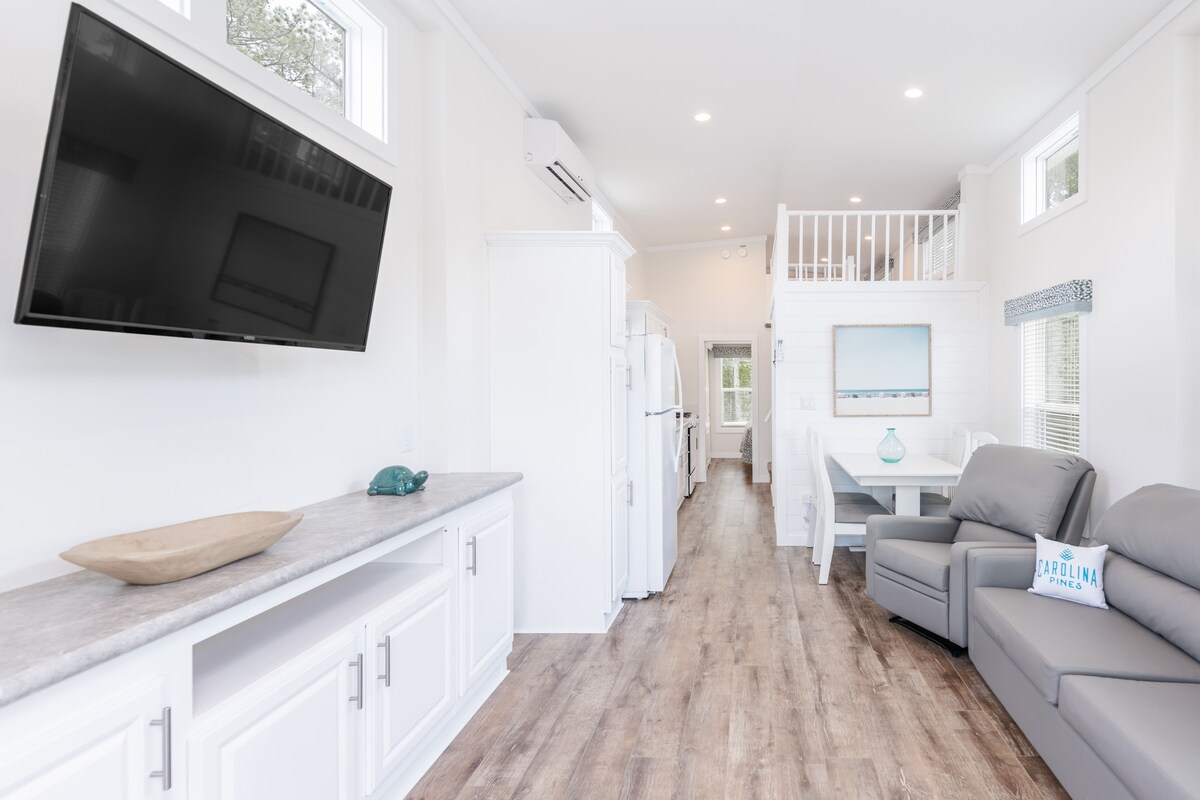 A modern kitchen with white cabinetry, a large TV, and a wooden bowl on the counter.