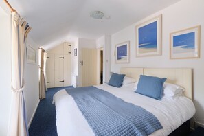 A hotel room with a large bed, a blue quilted bedspread, and two framed pictures on the wall. - A charming and spacious cottage in rural St Ives (Cornwall)