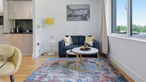 A modern living room with a sofa, coffee table, and a view of the city through a large window. - Cosy Studio Apartment in Canary Wharf (London)