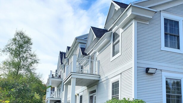 A row of white two-story houses with a covered front porch and a small garden.