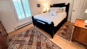 A bedroom with a bed, a nightstand, a lamp, a door, and a window with blinds.