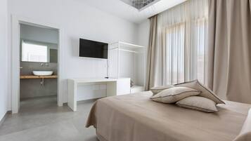 A modern bedroom with a bed, a desk, a TV, and a bathroom visible through an open door.