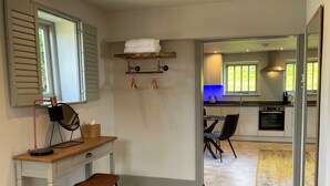 Eine moderne Küche mit Essbereich, ein kleiner Schreibtisch mit Lampe und Blick durch eine geöffnete Tür.