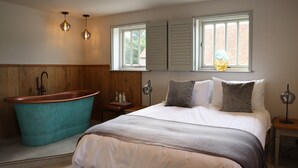 Ein Schlafzimmer mit einer Badewanne, einem Bett mit gemusterten Kissen und zwei Pendelleuchten.