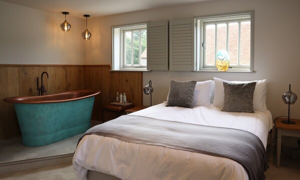Une chambre avec une baignoire, un lit agrémenté d’oreillers à motifs et deux lampes suspendues.