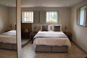 Une chambre avec deux lits, une fenêtre avec des volets, un miroir et une table de chevet avec une lampe.