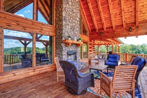 Una terraza de madera con pilares de piedra, mobiliario exterior y una chimenea.