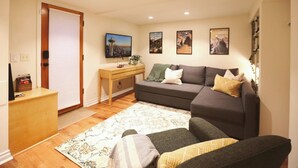 A living room with a sofa, a coffee table, a TV, and a desk with a computer. - Queen Anne Burrow: spacious studio & free bus pass (Seattle)