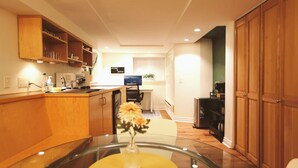 A compact kitchen with wooden cabinets, a dining table with a vase, and a computer desk. - Queen Anne Burrow: spacious studio & free bus pass (Seattle)