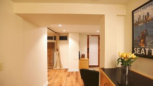 A hotel reception area with a wooden floor, a black chair, a vase with yellow flowers, and a framed picture on the wall. - Queen Anne Burrow: spacious studio & free bus pass (Seattle)