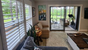 A living room with a sofa, a coffee table, a painting, and a sliding glass door leading to an outdoor patio. - Modern Beach Elegance: The Maples Retreat (Sunset Beach)