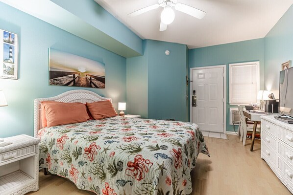 A bedroom with a bed, a desk, a chair, a ceiling fan, and a door.