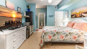 A bedroom with a bed, a ceiling fan, a dresser, a TV, and artwork on the walls.