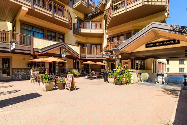 A multi-story hotel with outdoor seating and a sign for shops/restaurants.