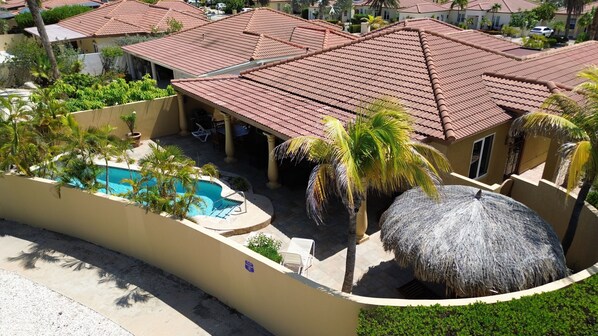 Zona residencial con piscina, palmeras y una estructura de techo de paja.