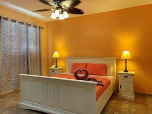 A bedroom with a bed, two bedside tables, a ceiling fan, and a patterned curtain.