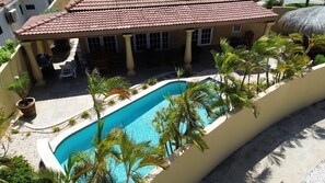 A pool surrounded by palm trees and a building with a tiled roof.