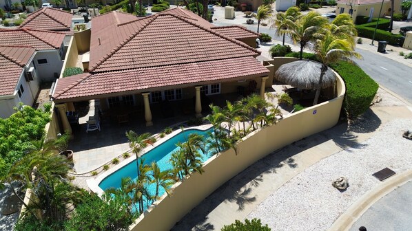 A residential area with a swimming pool, palm trees, and a building with a red-tiled roof.