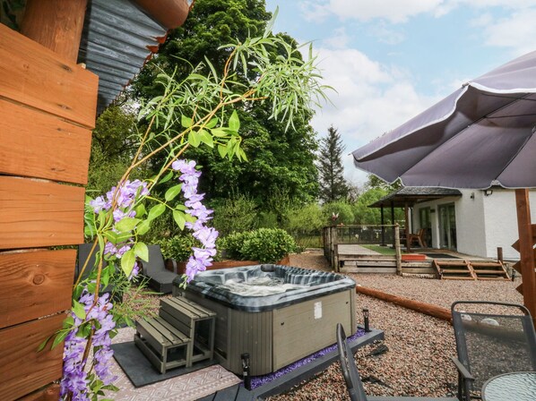 Un bain à remous dans un jardin doté d’une terrasse en bois, entouré de verdure et agrémenté d’un espace salon abrité.