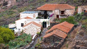Un pueblo en la ladera con edificios de piedra tradicionales, jardines en terrazas y un camino estrecho.