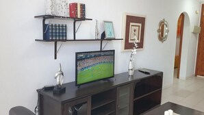 Ett vardagsrum med en tv-apparat på ett träställ, hyllor med böcker och dekorativa föremål samt en dörr med en träram.