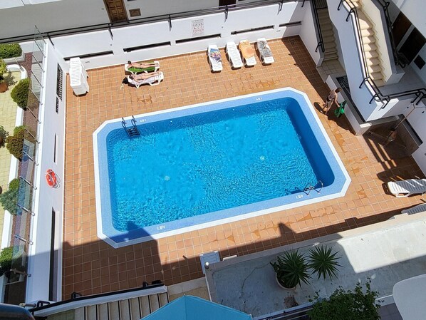 Piscina no terraço com superfície de água azul cristalina, rodeada por espreguiçadeiras e um pequeno deck.